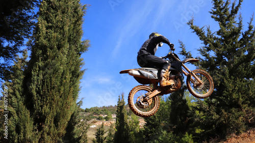 Professional dirt bike motocross rider performing stunts and flying from jump in extreme terrain track