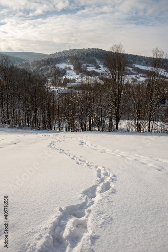 Beautiful winter landscape with mountains in the background. Footprints in the snow. Malastow village, Low Beskids, Poland. Selective focus. 