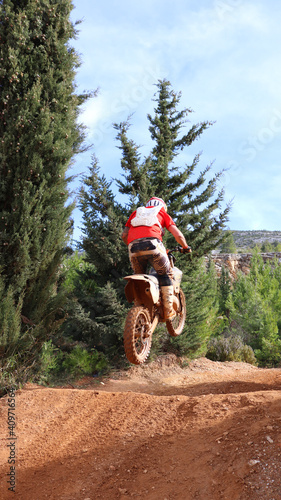 Professional dirt bike motocross rider performing stunts and flying from jump in extreme terrain track