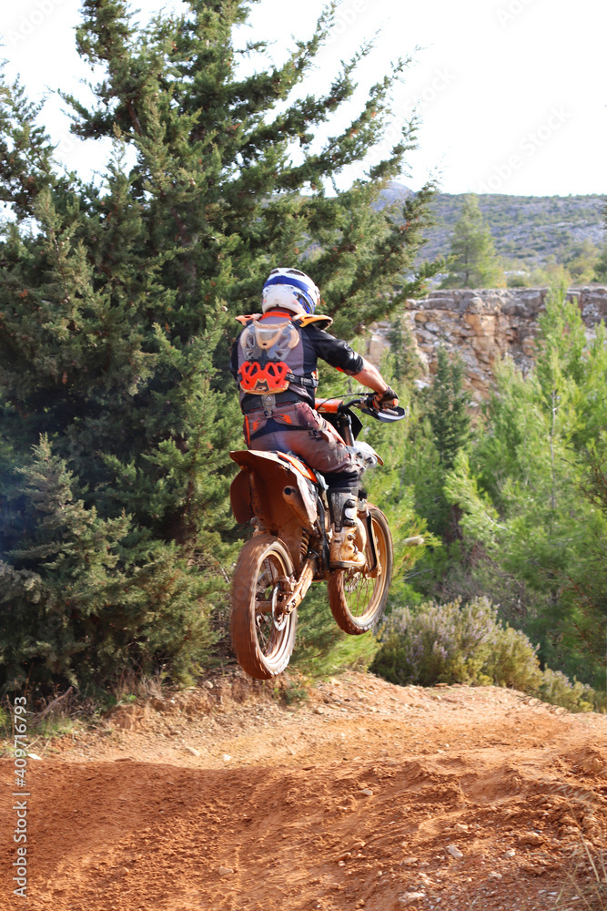 Professional dirt bike motocross rider performing stunts and flying from jump in extreme terrain track