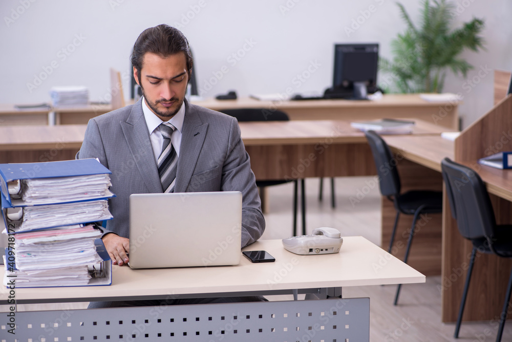 Young male employee unhappy with excessive work in the office Young male employee unhappy with excessive work in the office