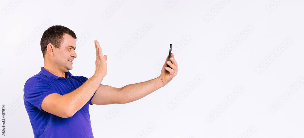 Banner,long format. A deaf man with a hearing aid waves his hand in front of the camera while communicating through social networks via a smartphone. White background and empty side space. Banner,long format. A deaf man with a hearing aid waves his hand in front of the camera while communicating through social networks via a smartphone. White background and empty side space.
