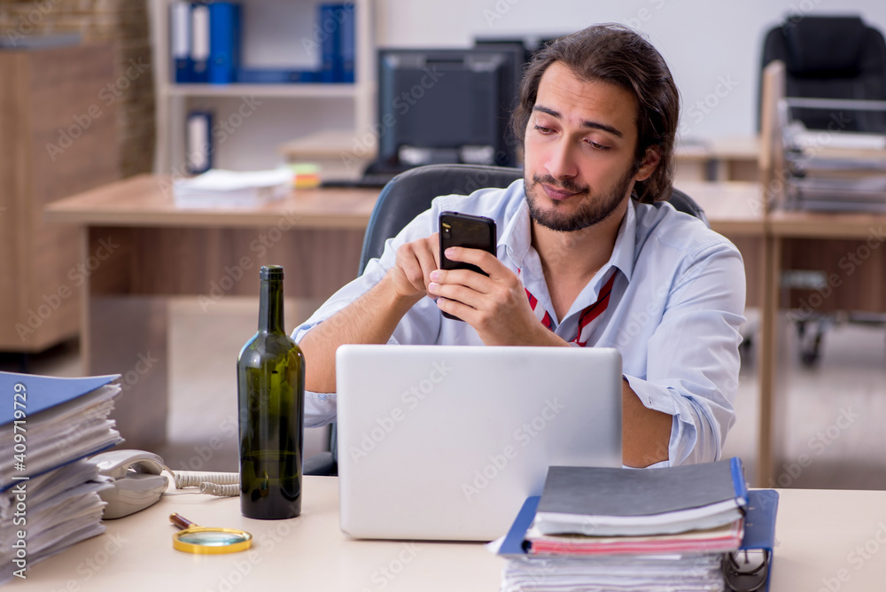 Young male employee drinking alcohol in the office Young male employee drinking alcohol in the office