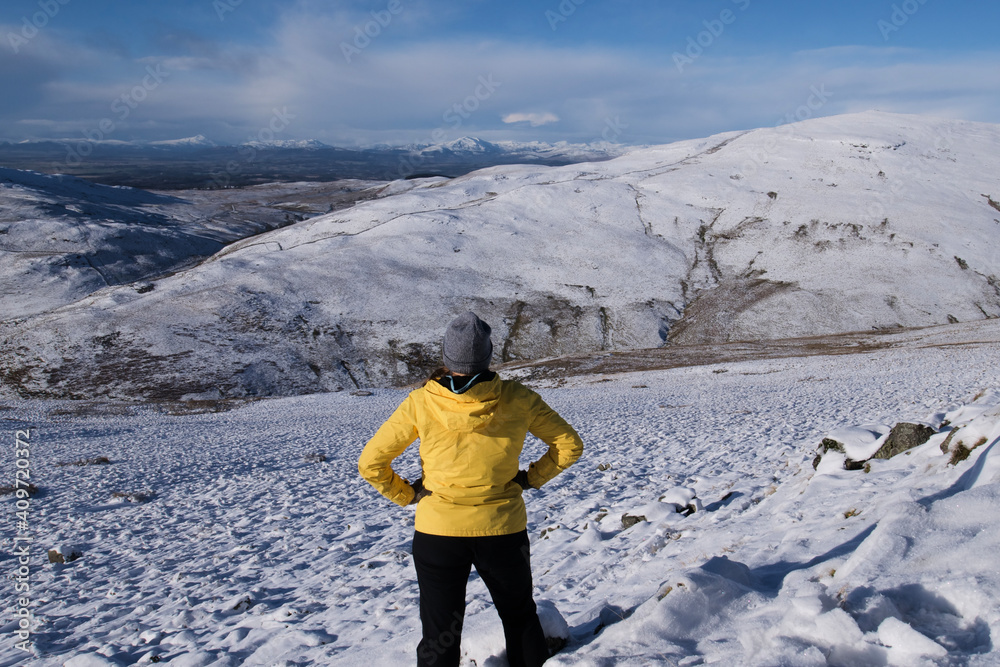 hiker woman in winter Scottish Hills wearing a yellow jacket enjoying the view