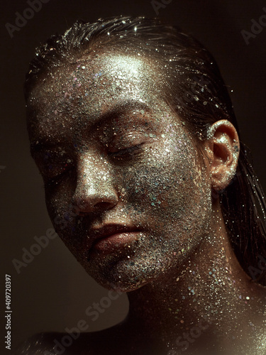 Glittering silver make up on female face, young beautiful girl with wet hair and sparkling body art, close up portrait