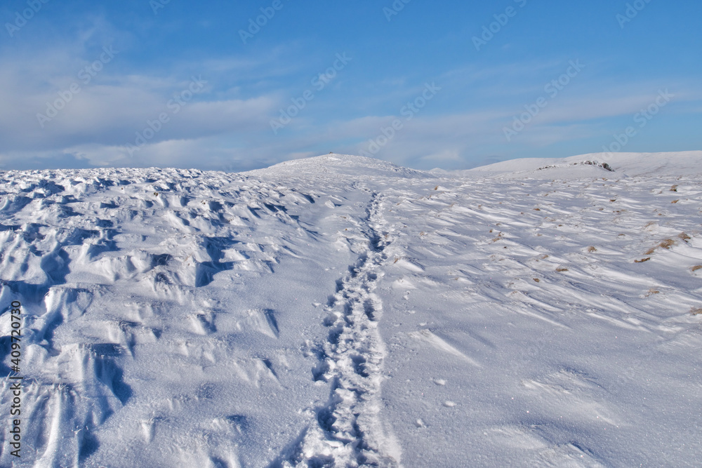 Path in snow leading to the peak of a snow covered mountain in winter