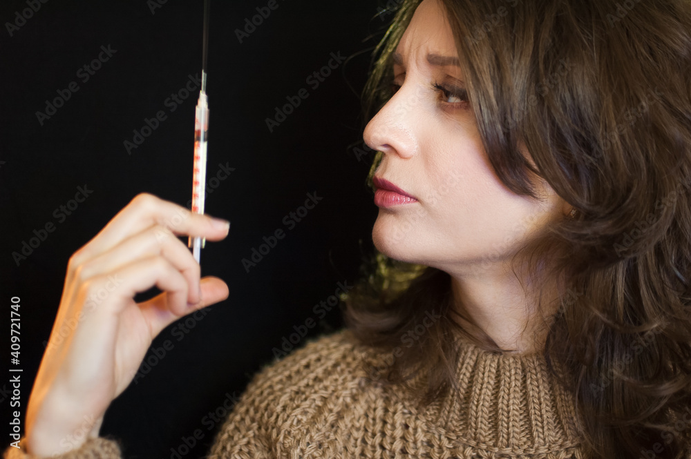 Obraz premium Vaccine concept. Female portrait of caucasian girl holding a syringe and looking at it on black background in studio.