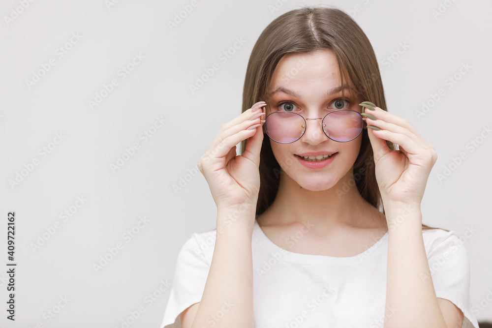 smiling frowning office girl staring at camera through eyeglasses on white background. Young woman adjusting eyewear. Glasses wearing concept