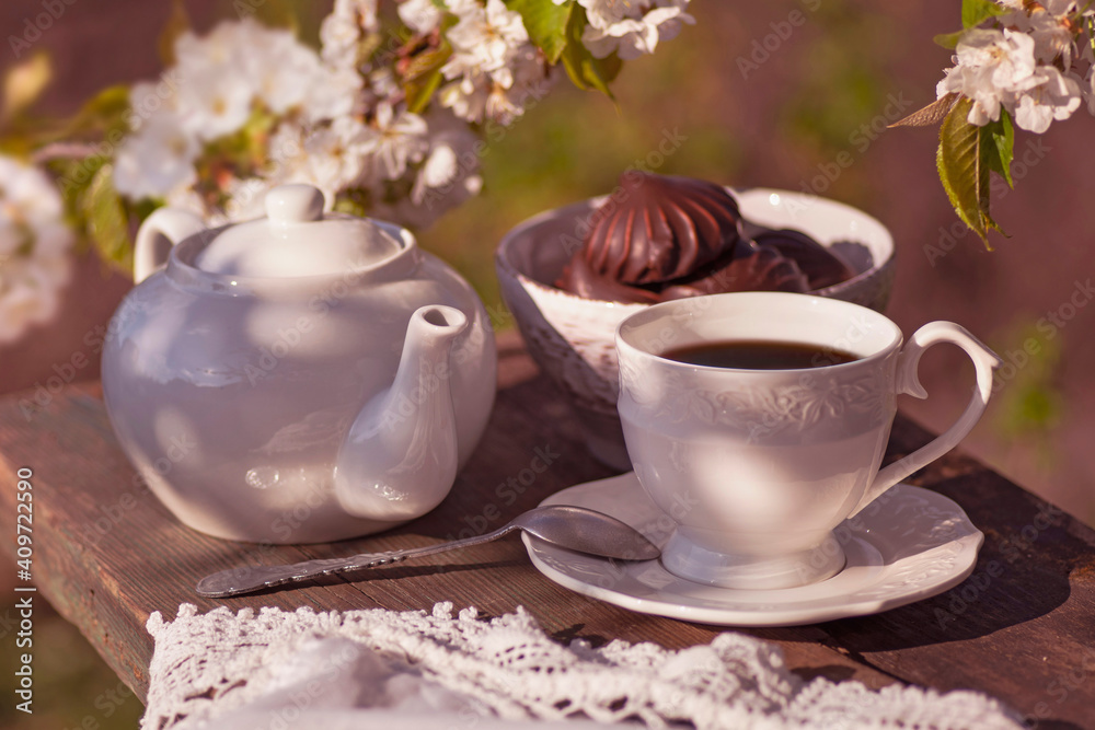 tea set, white tablecloth on a sunny day, cherry blossom branches, marshmallows in chocolate, wooden table. Outdoor breakfast, picnic, brunch, spring mood. Soft focus tea set, white tablecloth on a sunny day, cherry blossom branches, marshmallows in chocolate, wooden table. Outdoor breakfast, picnic, brunch, spring mood. Soft focus