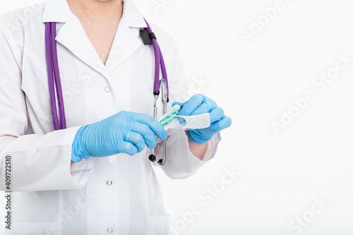 A young nurse in a mask opens a syringe on a white background in a white coat, to make a vaccination, an injection. The concept of vaccination and protection against influenza, from avid, copy space