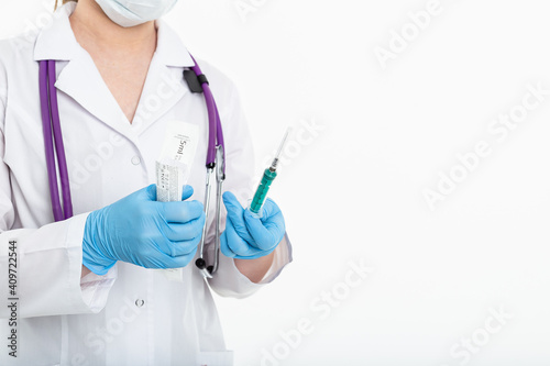 A young nurse in a mask opens a syringe on a white background in a white coat, to make a vaccination, an injection. The concept of vaccination and protection against influenza, from avid, copy space