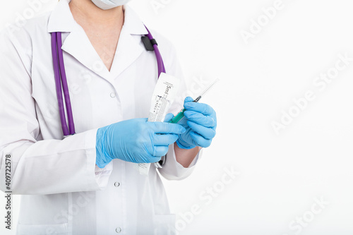A young nurse in a mask opens a syringe on a white background in a white coat, to make a vaccination, an injection. The concept of vaccination and protection against influenza, from avid, copy space