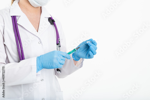 A young nurse in a mask opens a syringe on a white background in a white coat, to make a vaccination, an injection. The concept of vaccination and protection against influenza, from avid, copy space