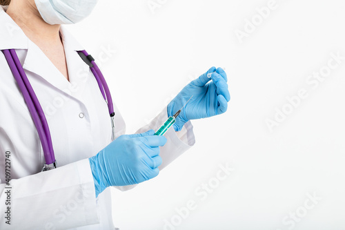 A young nurse in a mask opens a syringe on a white background in a white coat, to make a vaccination, an injection. The concept of vaccination and protection against influenza, from avid, copy space