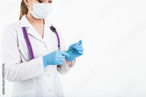 A young nurse in a mask opens a syringe on a white background in a white coat, to make a vaccination, an injection. The concept of vaccination and protection against influenza, from avid, copy space