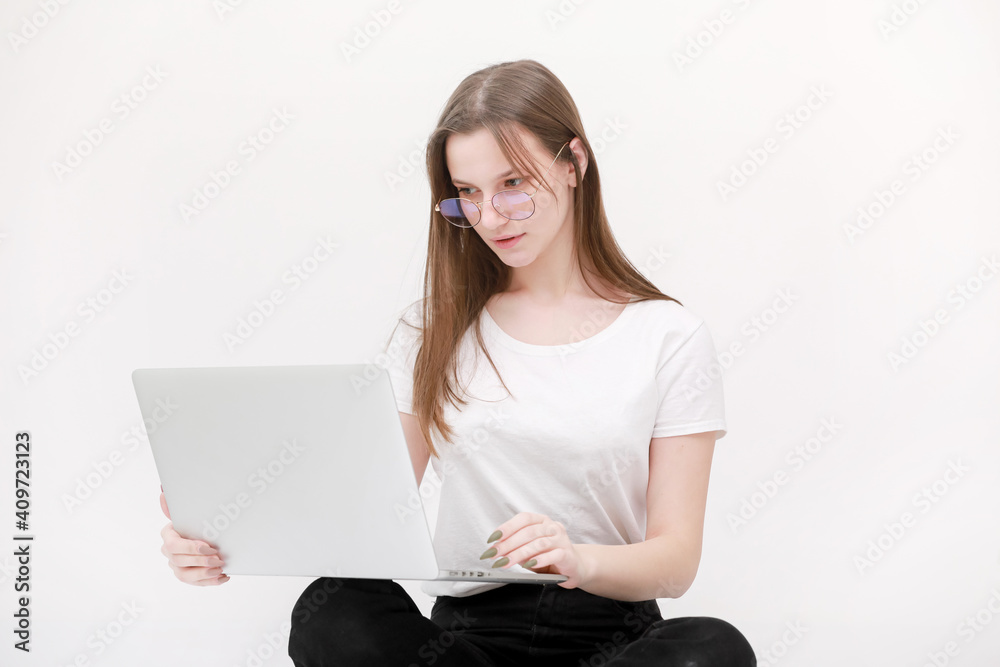 Portrait of a beautiful young girl with blond hair in glasses and a white T-shirt working or studying on a laptop isolated on a white background. Concept of business woman. Casual blogger woman Portrait of a beautiful young girl with blond hair in glasses and a white T-shirt working or studying on a laptop isolated on a white background. Concept of business woman. Casual blogger woman
