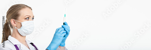 Young nurse in a mask dials the vaccine into a syringe while sitting in a hospital next to a patient. Female patient waiting for flu injection. Concept of vaccination and protection against influenza