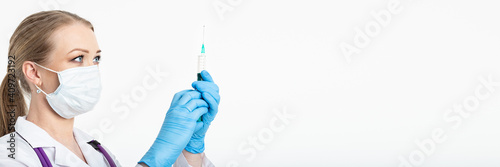Young nurse in a mask dials the vaccine into a syringe while sitting in a hospital next to a patient. Female patient waiting for flu injection. Concept of vaccination and protection against influenza