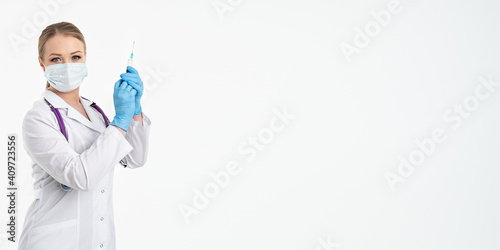 A young nurse in a mask and white coat holds a syringe with a needle for injections, flu shots, covid. The concept of vaccination and protection against influenza, from a pandemic. copy space. banner