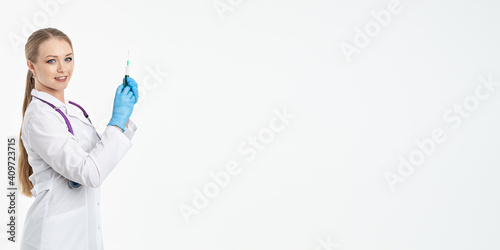 A young nurse in a mask and white coat holds a syringe with a needle for injections, flu shots, covid. The concept of vaccination and protection against influenza, from a pandemic. copy space. banner