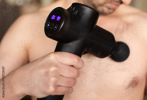 Man massaging himself with massage percussion device after workout.