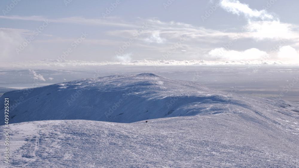 silhouette of an alone walker on top of a snow covered hill in Scotland