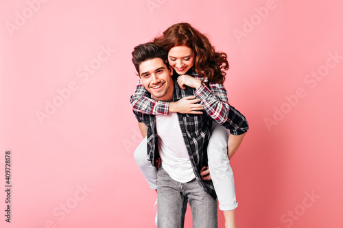 Ginger girl embracing boyfriend. Studio shot of funny couple isolated on pink.