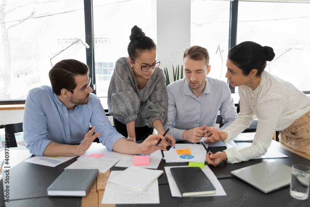 Multiethnic team of colleagues brainstorming over documents, sharing ideas, discussing sales results statistics. Employees working on project tasks, together, meeting and talking. Cooperation concept