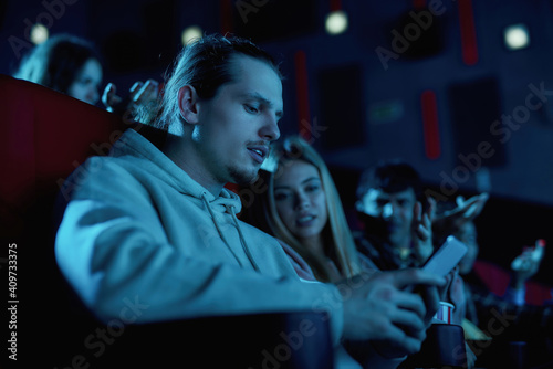 Focused young guy using his smartphone while having a movie date at the cinema