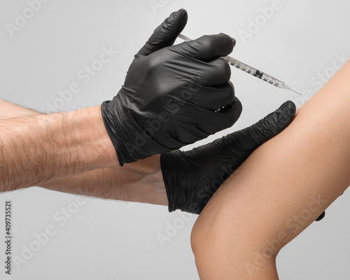 A male doctor wearing latex black gloves gives the vaccination to the patient in the shoulder, using a 1ml disposable syringe, close up. photo