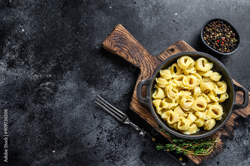 Italian tortellini pasta with cheese sauce in a pan. Black background. Top view. Copy space photo