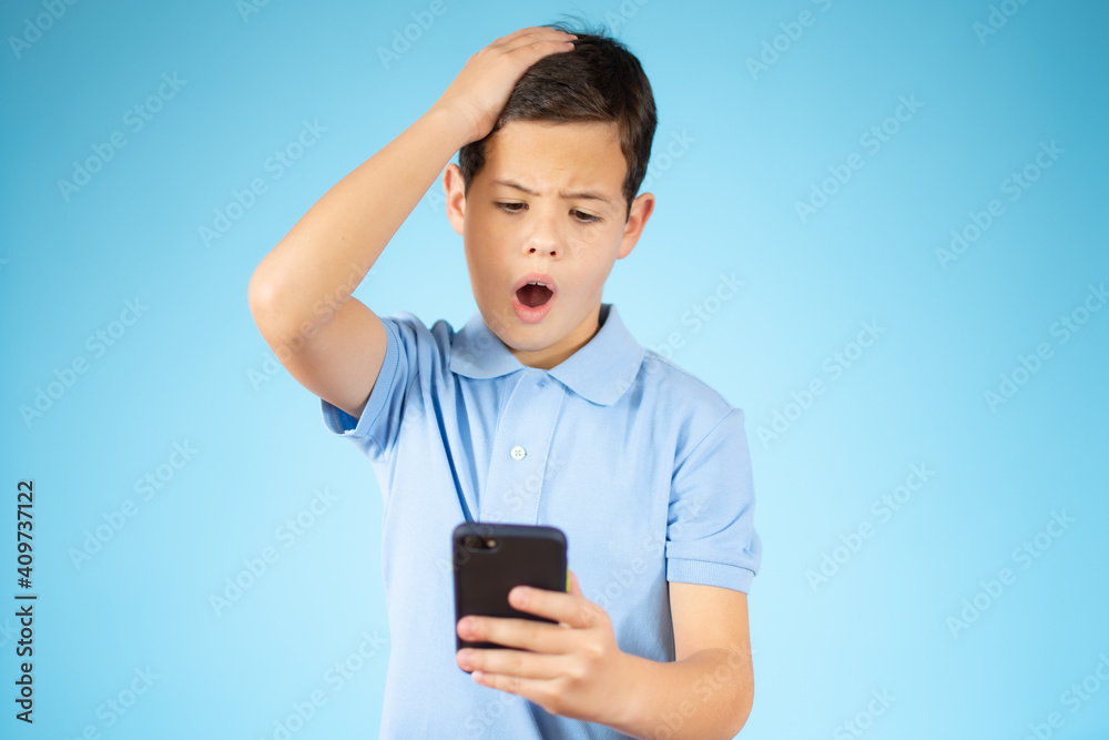 Cute ginger kid with mobile phone on blue studio background, using exciting mobile applications or chatting with friends, copy space. Cute ginger kid with mobile phone on blue studio background, using exciting mobile applications or chatting with friends, copy space.