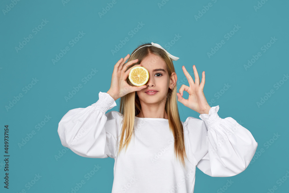adorable little child girl holding fresh juicy lemon and showing Ok gesture isolated over blue background adorable little child girl holding fresh juicy lemon and showing Ok gesture isolated over blue background