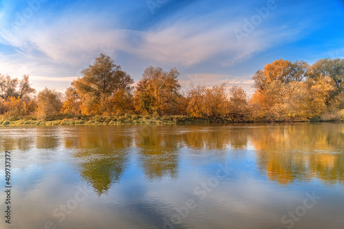 Beautiful violin shaped pier at autumn sunset over the river with reflected orange and green trees, clouds and blue sky