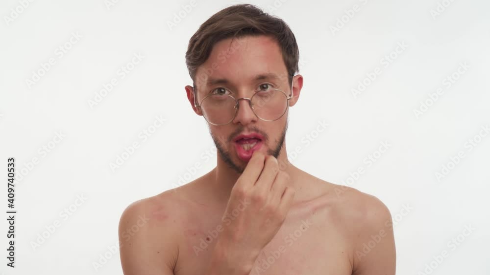 One young metrosexual Caucasian half naked sexy bearded man with brown hair wear silver glasses, stare camera like mirror, holds in hand, puts pink lipstick on his lips isolated on white background. One young metrosexual Caucasian half naked sexy bearded man with brown hair wear silver glasses, stare camera like mirror, holds in hand, puts pink lipstick on his lips isolated on white background.