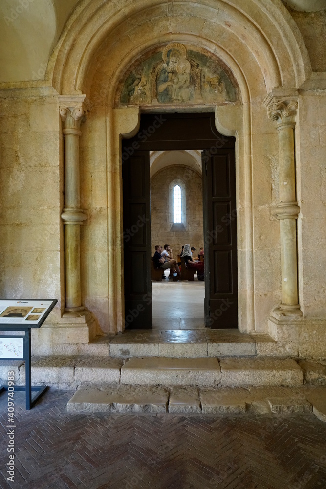 abbazia , colonne di pietra che incorniciano porta antica con all' interno fedeli che pregano , finestra sullo sfondo 