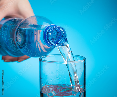 Pouring water into a glass on a light blue background. Close-up, Side view. The concept of drinking water.