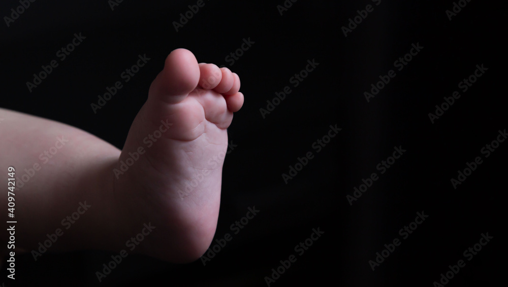 Leg of a light-skinned baby on a black background. Place for an inscription. Abortion. Motherhood. Part of the body. The close plan. Advertising. Maternity hospital. Birth. Baby. Adoption. Leg of a light-skinned baby on a black background. Place for an inscription. Abortion. Motherhood. Part of the body. The close plan. Advertising. Maternity hospital. Birth. Baby. Adoption.