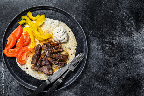 Tortilla with beef meat steak and fresh salad on a rustic plate. Black background. Top view. Copy space
