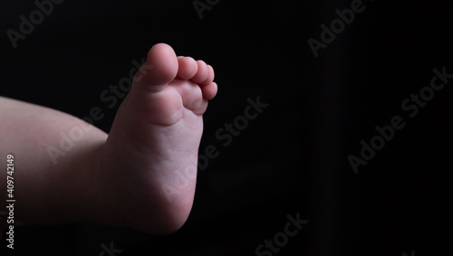 Leg of a light-skinned baby on a black background. Place for an inscription. Abortion. Motherhood. Part of the body. The close plan. Advertising. Maternity hospital. Birth. Baby. Adoption.