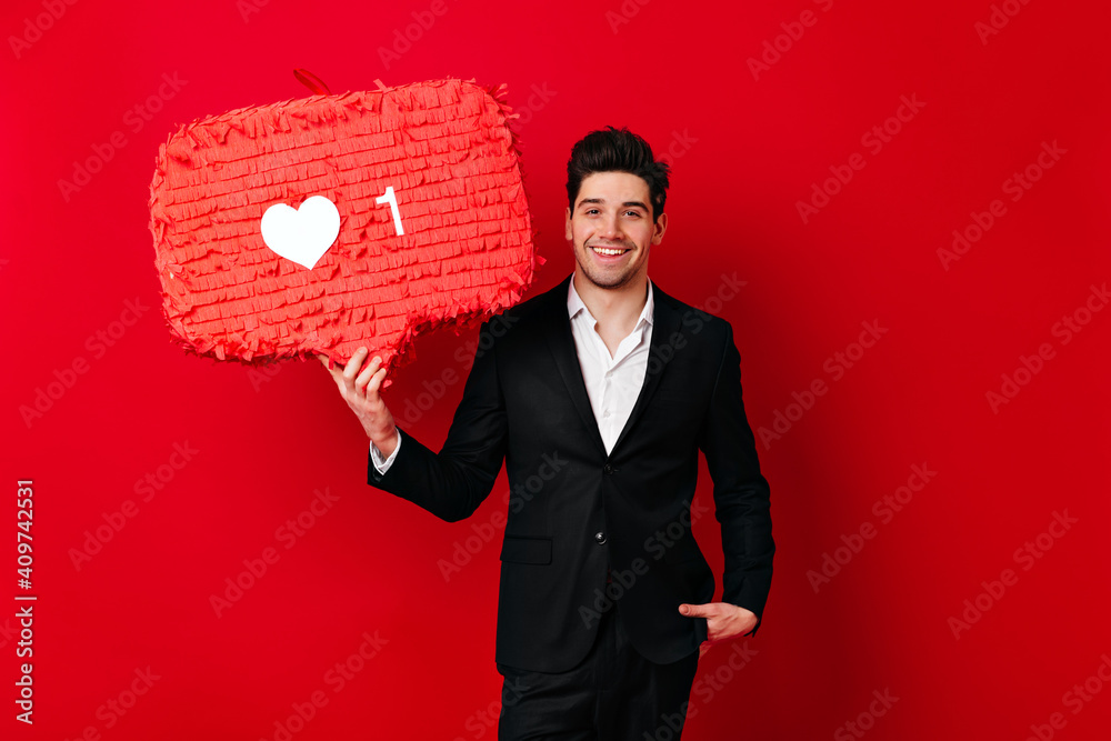 Confident man in suit posing with heart icon. Studio shot of cheerful male model celebrating valentine's day. Confident man in suit posing with heart icon. Studio shot of cheerful male model celebrating valentine's day.