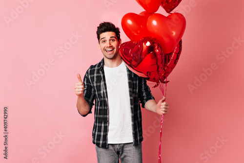 Cheerful man in checkered shirt holding valentine balloons. Studio shot of excited male model isolated on pink.