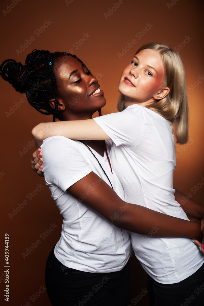 Obraz premium two pretty girls african and caucasian blond posing cheerful together on brown background, etnithity diverse lifestyle people concept