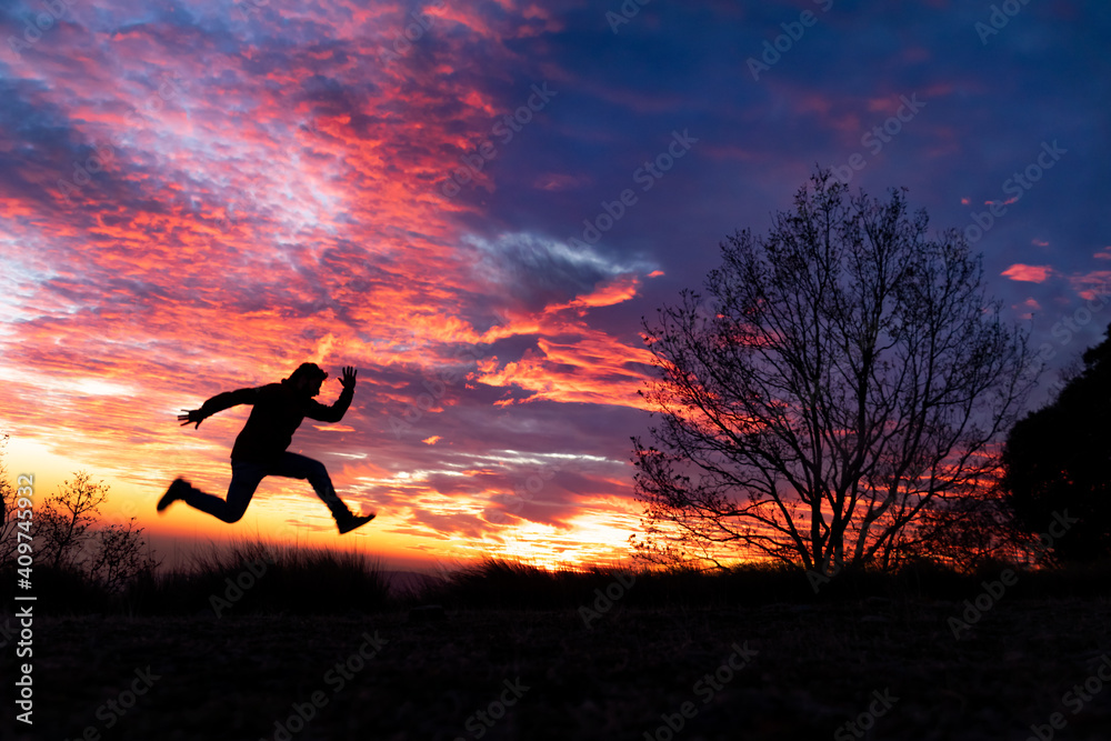 Fondo de atardecer rojo y azul con un arbol y la silueta de un hombre saltando corriendo 