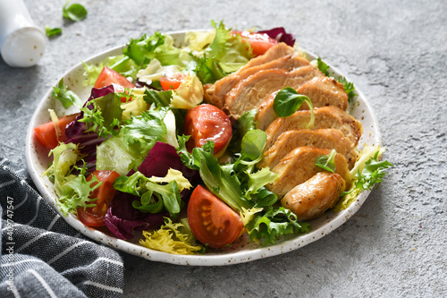 Mix salad with tomatoes and chicken fillet in a plate on a concrete background.