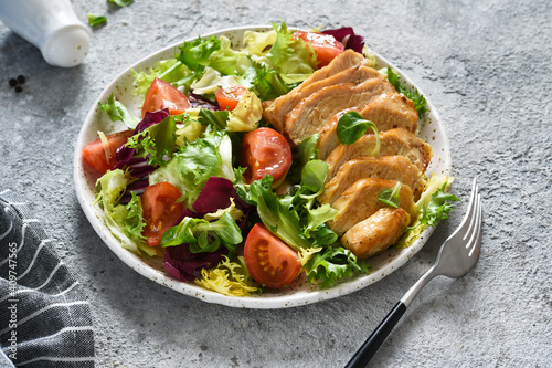 Mix salad with tomatoes and chicken fillet in a plate on a concrete background.