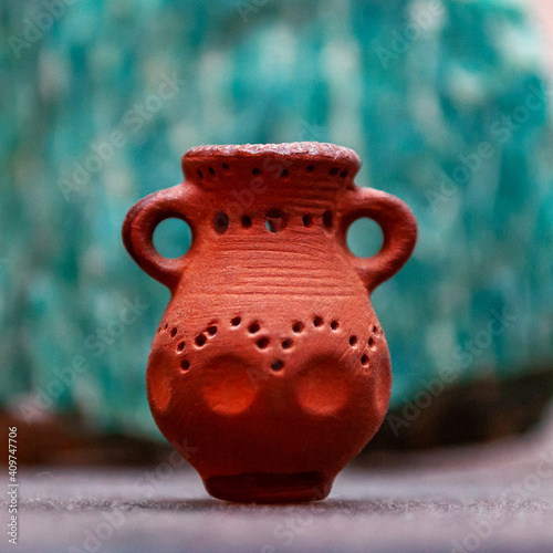 The homemade clay pot of bright orange color on a blurred background of light green stone, with shapes gradually eroding from center to edge