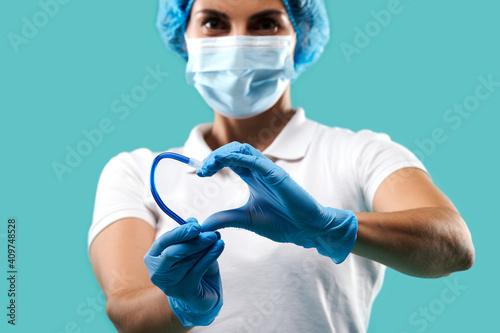 Young dentist woman wearing medical uniform holding a saliva ejector and showing a shape of heart . Portrait on blue background
