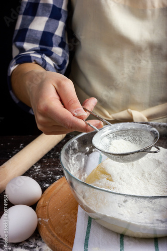 A woman is sifting flour through a sieve. Cooking dough for baking. Yeast dough.