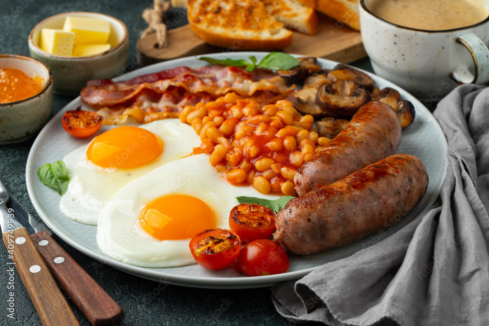 Full English breakfast on a plate with fried eggs, sausages, bacon, beans, toasts and coffee on dark stone background Full English breakfast on a plate with fried eggs, sausages, bacon, beans, toasts and coffee on dark stone background